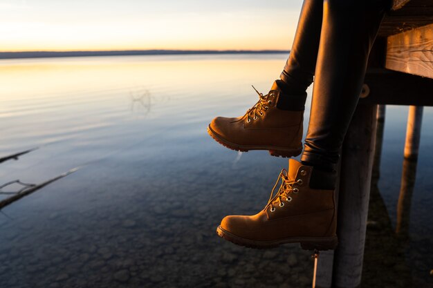 Niña con botas sentado en un muelle durante la puesta de sol