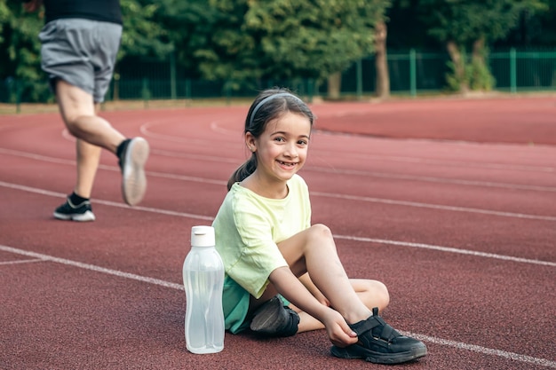 Foto gratuita una niña con una botella de agua sentada en una pista de atletismo