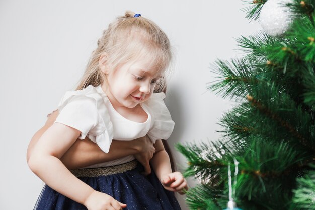 Niña en brazo decorando árbol de navidad