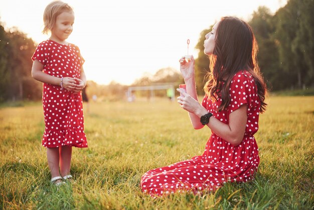 Niña con burbujas con su madre en el parque al atardecer.