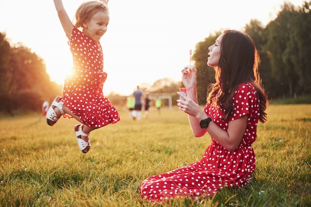 Niña con burbujas con su madre en el parque al atardecer.