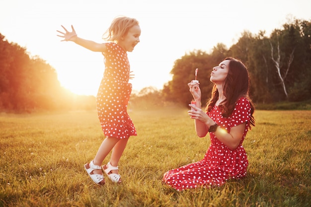 Niña con burbujas con su madre en el parque al atardecer.