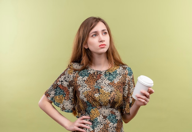 Niña con cabello largo vistiendo coloridos vestidos sosteniendo la taza de café mirando a un lado disgustado