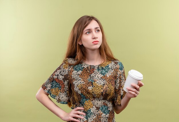 Niña con cabello largo vistiendo coloridos vestidos sosteniendo la taza de café mirando a un lado disgustado