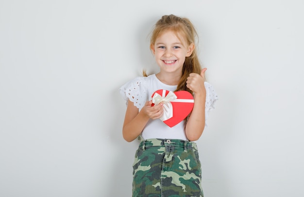 Niña con caja de regalo con el pulgar hacia arriba en camiseta blanca