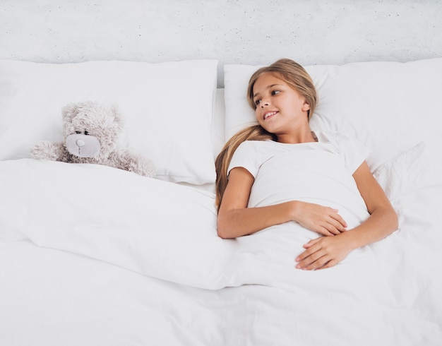 Foto gratuita niña en la cama con su osito de peluche