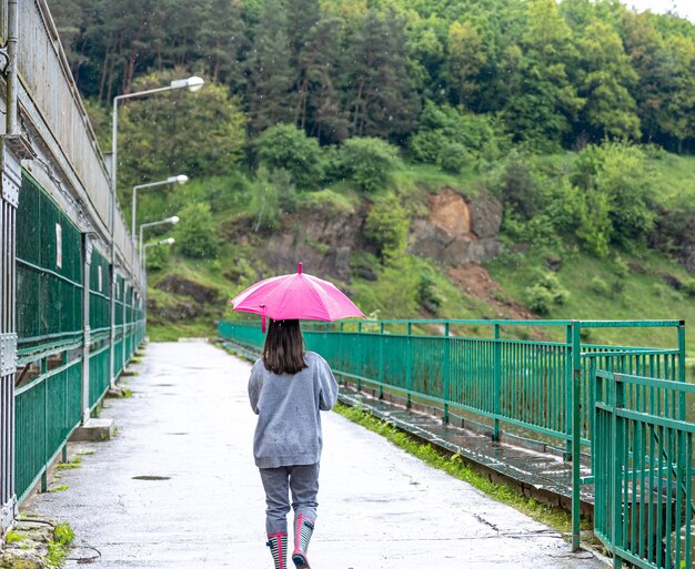 Una niña camina bajo un paraguas en tiempo lluvioso en un puente en el bosque