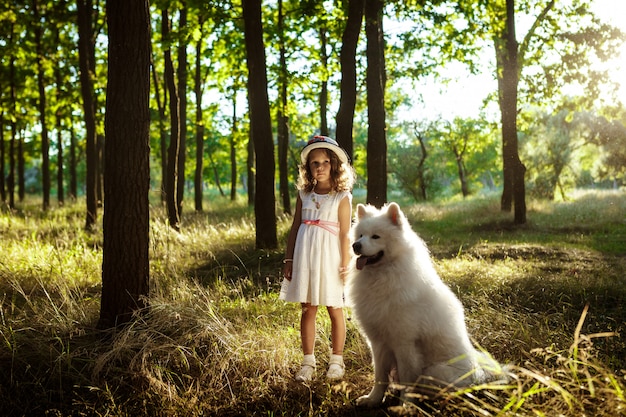 Niña caminando, jugando con el perro en el parque al atardecer.