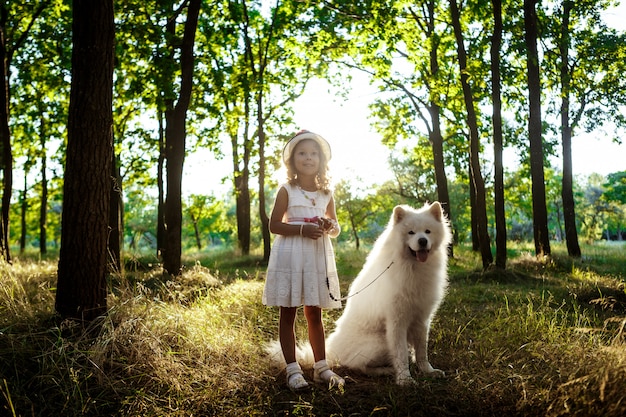 Niña caminando, jugando con el perro en el parque al atardecer.