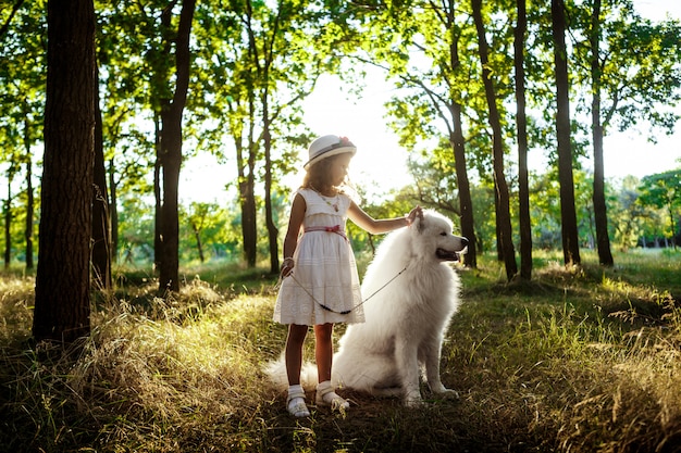 Niña caminando, jugando con el perro en el parque al atardecer.