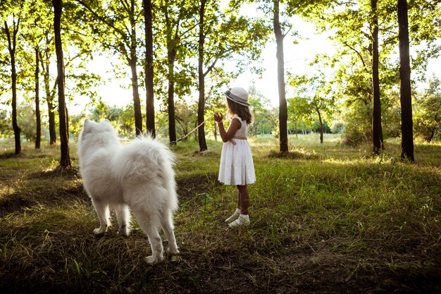 Niña caminando, jugando con el perro en el parque al atardecer.