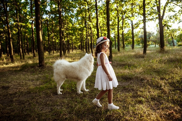 Niña caminando, jugando con el perro en el parque al atardecer.