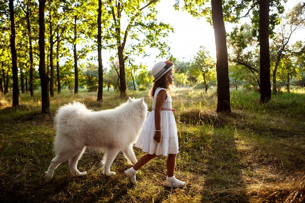 Niña caminando, jugando con el perro en el parque al atardecer.