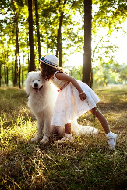 Niña caminando, jugando con el perro en el parque al atardecer.