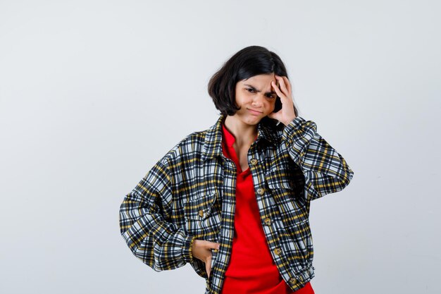 Niña en camisa, chaqueta que sufre de dolor de cabeza y luce dolorosa, vista frontal.