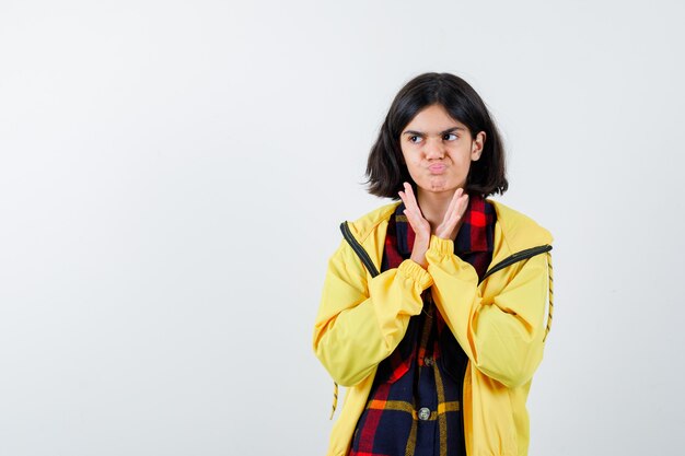 Niña en camisa a cuadros, chaqueta aplaudiendo y mirando vacilante