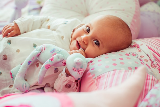 Niña en camisa manchada se encuentra entre las almohadas de color rosa