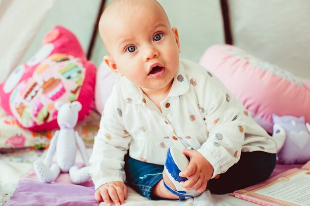 Niña en camisa manchada se sienta entre las almohadas de color rosa