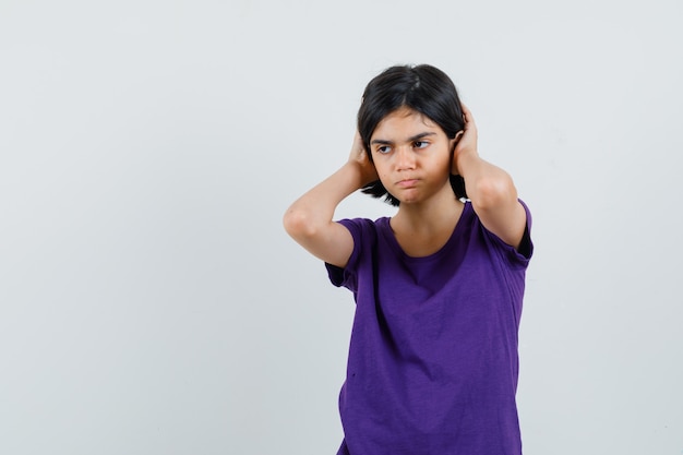 Niña en camiseta agarrando la cabeza entre las manos y mirando molesto,