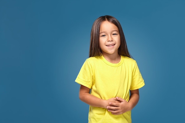 Niña en camiseta amarilla está sonriendo sobre fondo azul.