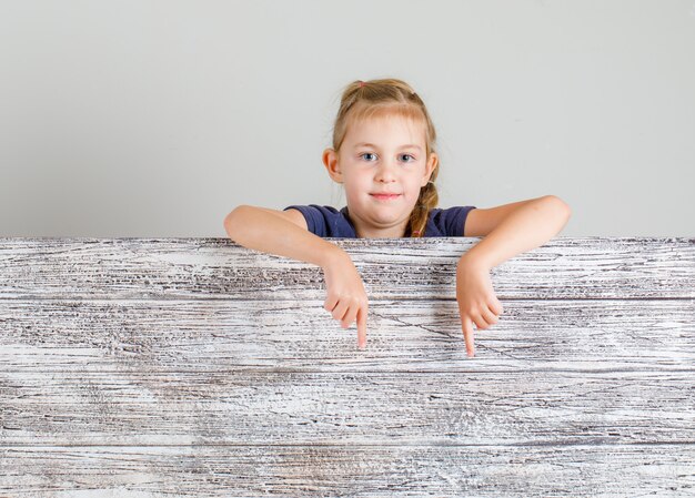 Niña en camiseta apuntando al espacio vacío y mirando positiva, vista frontal.