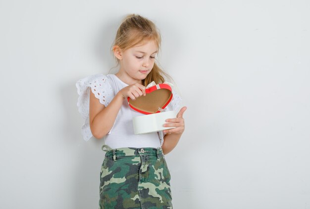 Niña con camiseta blanca, falda abriendo la caja actual y mirando con cuidado