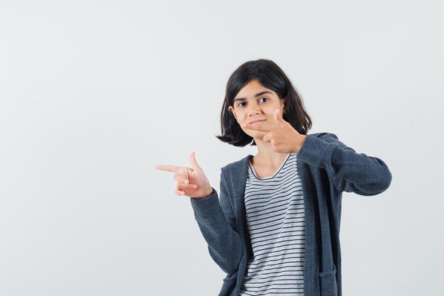 Niña en camiseta, chaqueta apuntando hacia el lado izquierdo y mirando confiada