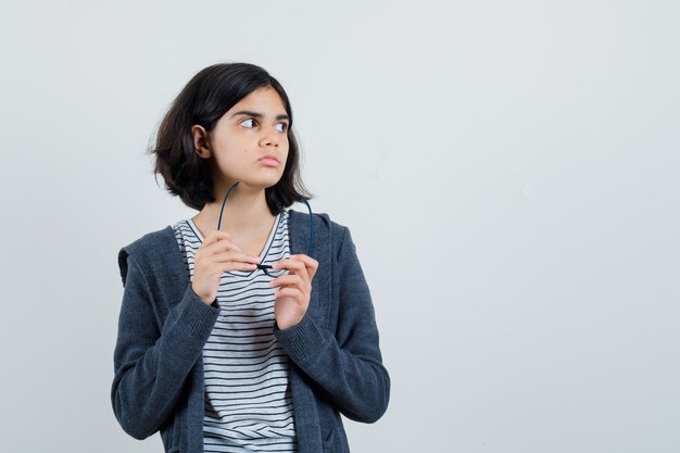 Niña en camiseta, chaqueta con gafas y mirando pensativo,