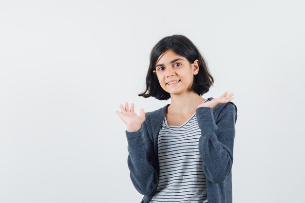 Niña en camiseta, chaqueta levantando las palmas abiertas y mirando alegre