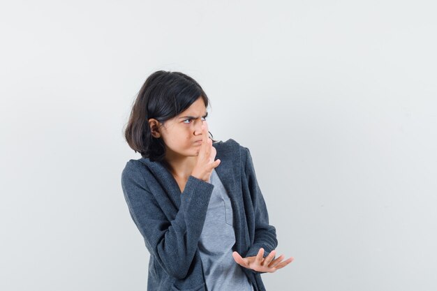 Niña en camiseta, chaqueta manteniendo las manos de manera protectora y mirando asustado, vista frontal.