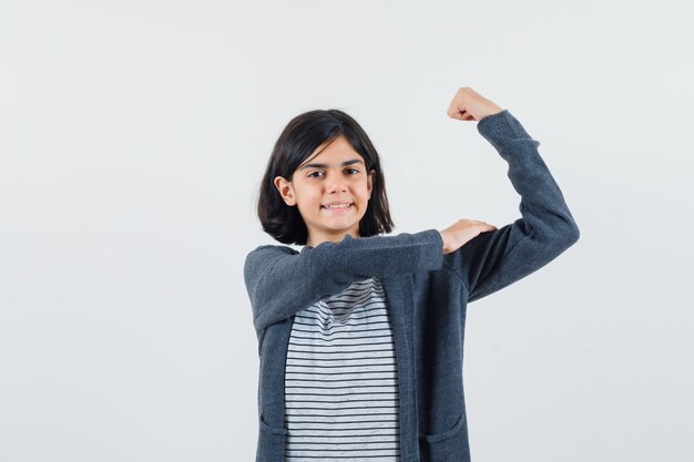 Niña en camiseta, chaqueta mostrando los músculos del brazo y mirando confiada