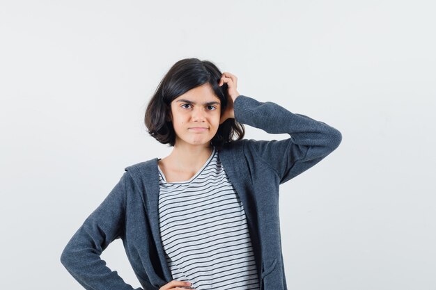 Niña en camiseta, chaqueta rascándose la cabeza y mirando pensativa