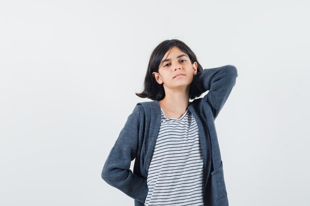 Niña en camiseta, chaqueta sosteniendo la mano en el cuello y mirando relajado