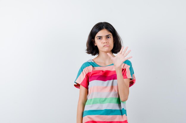 Niña en camiseta, jeans levantando la mano como para saludar a alguien, curvando los labios y mirando disgustado, vista frontal.