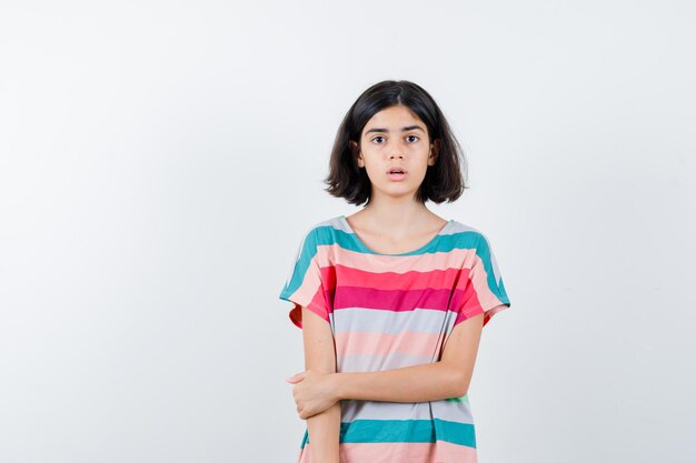 Niña en camiseta, jeans sosteniendo la mano en el brazo y mirando sorprendido, vista frontal.