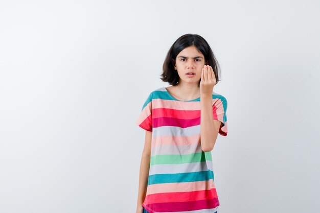 Niña en camiseta mostrando gesto italiano y mirando serio, vista frontal.