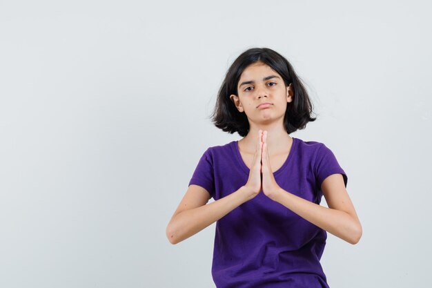 Niña en camiseta mostrando gesto de namaste y mirando molesto,