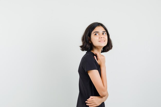 Niña en camiseta negra mirando hacia atrás sobre su hombro y con curiosidad.