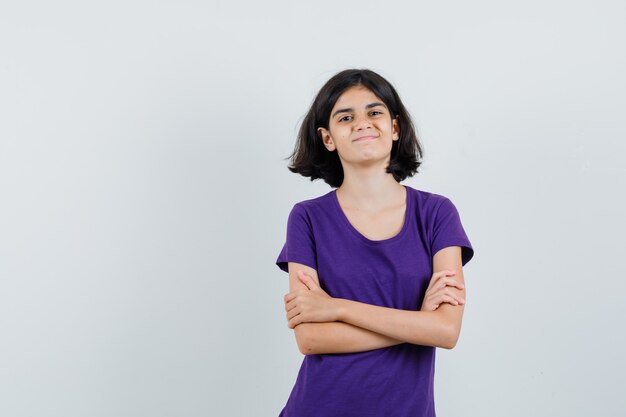 Niña en camiseta de pie con los brazos cruzados y mirando confiado,