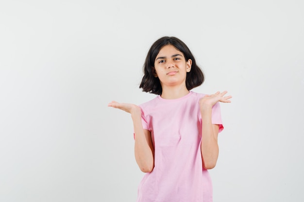 Niña en camiseta rosa gesticulando como mostrando o sosteniendo algo y mirando descontento, vista frontal.