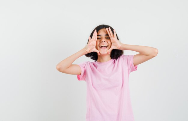 Niña en camiseta rosa gritando o anunciando algo y mirando feliz, vista frontal.