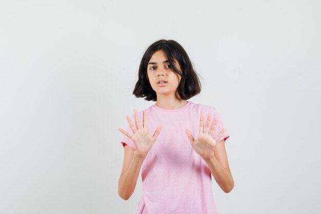 Niña en camiseta rosa mostrando gesto de rechazo y mirando asustada, vista frontal.