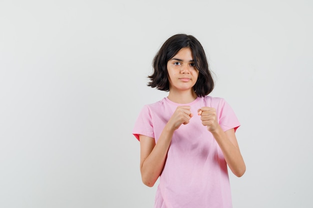 Niña en camiseta rosa de pie en pose de lucha y mirando confiado, vista frontal.