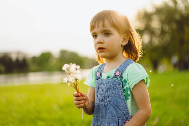 Foto gratuita niña en un campo de diente de león, al atardecer, niño feliz emocional.