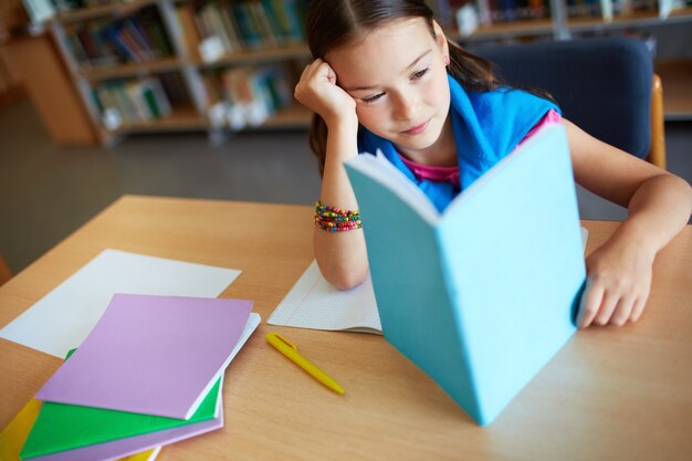 Niña cansada leyendo en la biblioteca