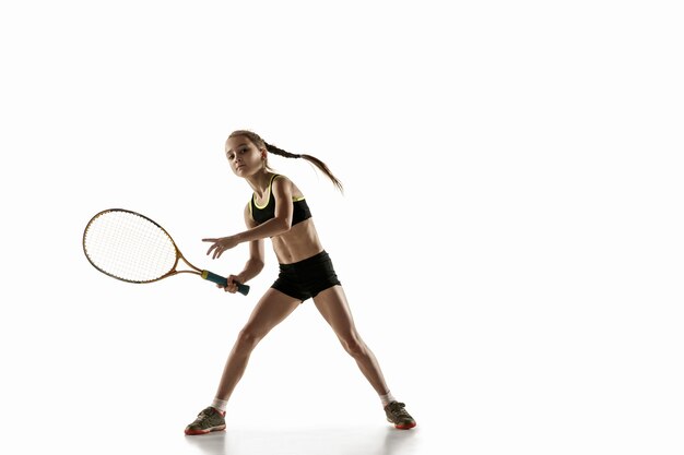 Niña caucásica jugando al tenis aislado en la pared blanca