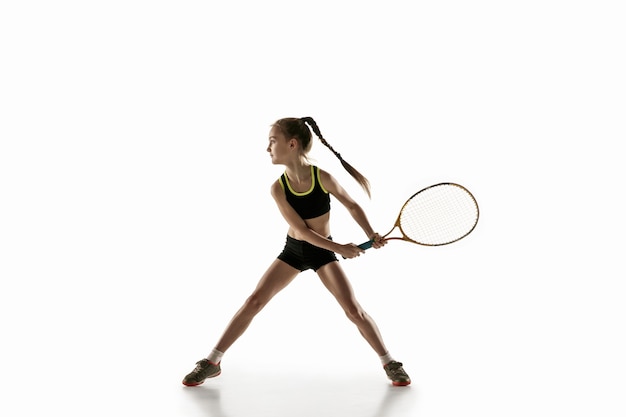 Niña caucásica jugando al tenis aislado en la pared blanca