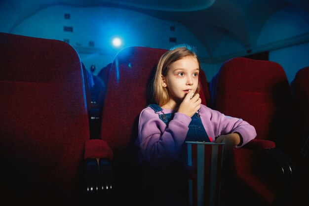 Niña caucásica viendo una película en un cine, una casa o un cine.