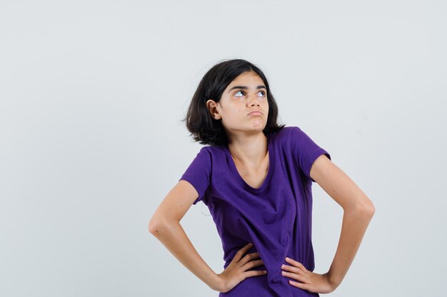 Niña cogidos de la mano en la cintura en camiseta y mirando vacilante,