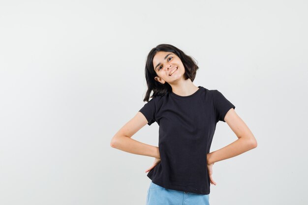 Niña cogidos de la mano en la cintura con camiseta negra, pantalones cortos y aspecto alegre. vista frontal.